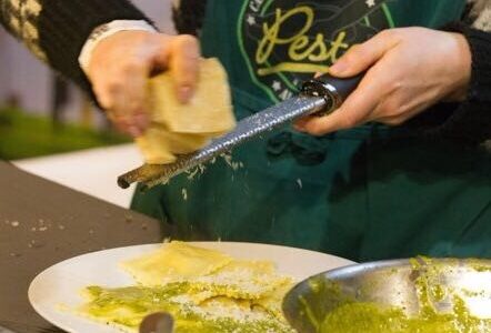 Hände beim Kochen von Pasta, die gerade Parmesankäse über die Pasta reiben